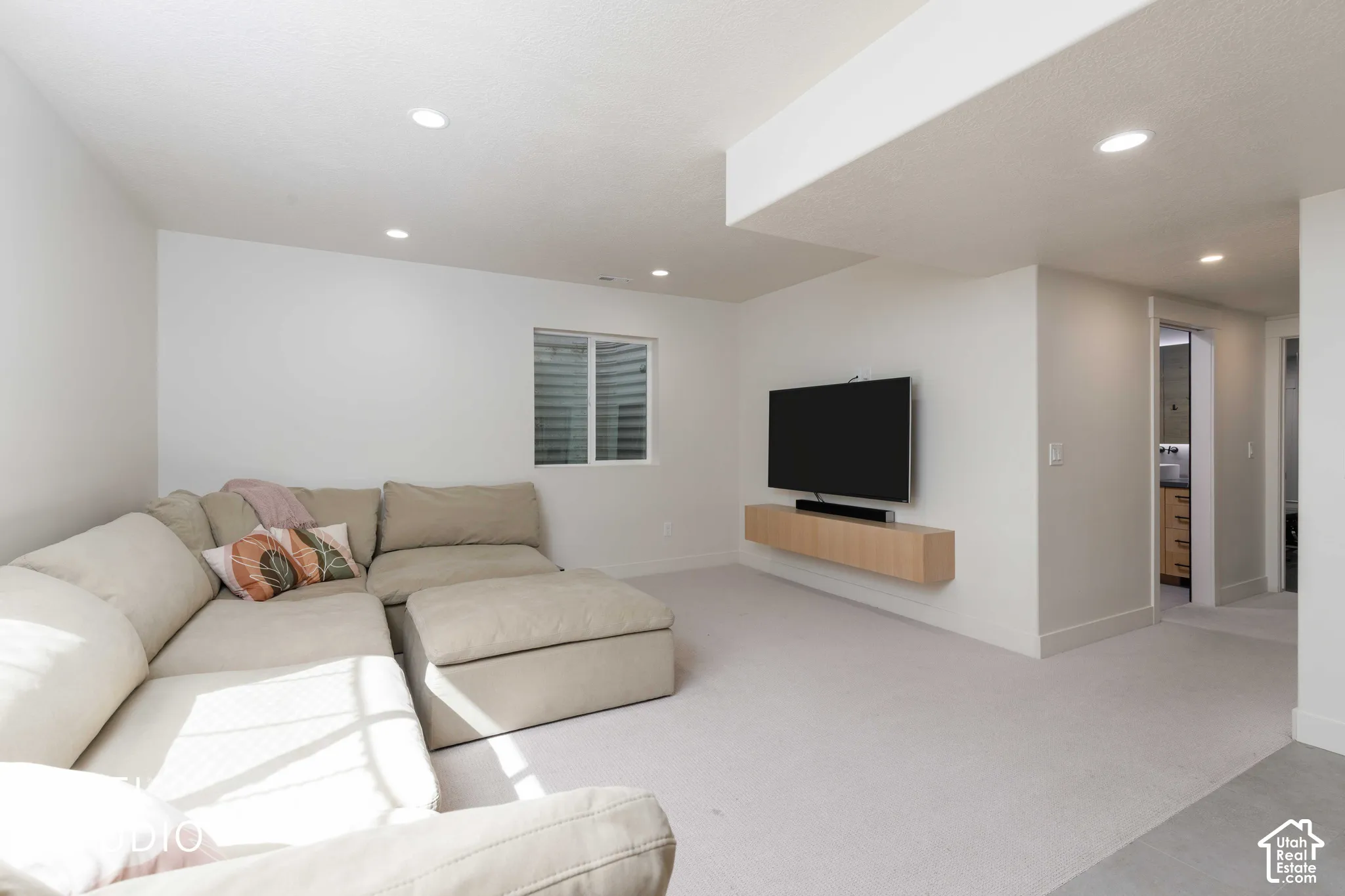 Recessed lighting throughout, carpet flooring, and a wall-mounted media console