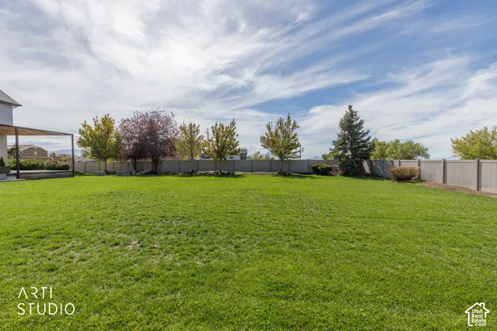 Expansive green lawn, perimeter fencing, mature trees, and a ground-level patio with a pergola structure