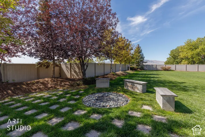 Expansive lawn with mature trees, a decorative rock fire pit, concrete benches, and geometric paver stepping stones