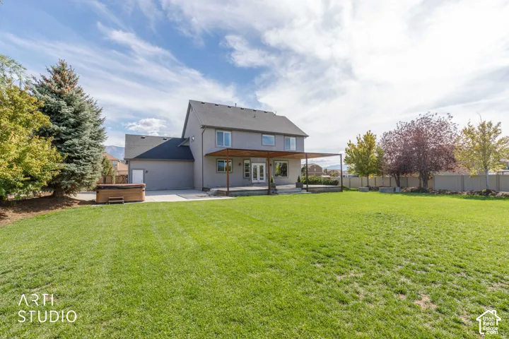 Expansive green lawn with mature trees, a two-story residence with a patio, and a hot tub on a concrete pad