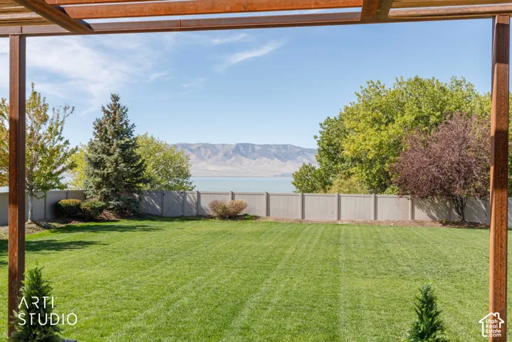 Expansive lawn with mature trees and shrubs, bordered by a privacy fence, with a distant body of water and mountains