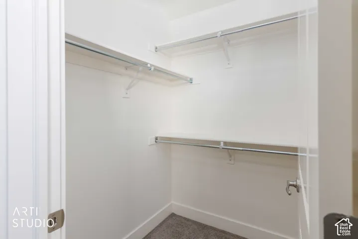 Walk-in closet featuring white painted walls and shelving, chrome hanging rods, and grey carpeting