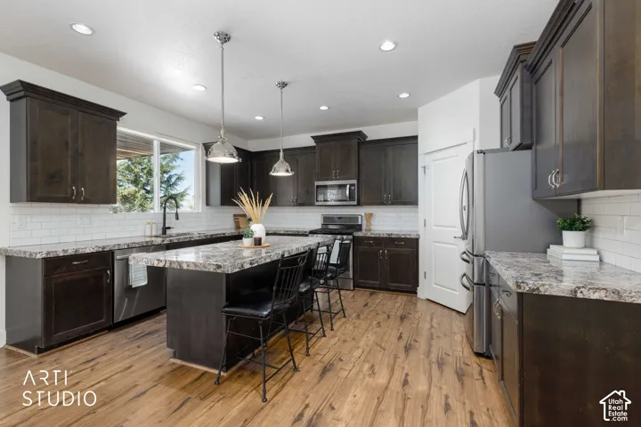 Kitchen featuring wood-finish flooring, dark wood-finish cabinetry, a large window, a center island with seating, and stainless steel appliances