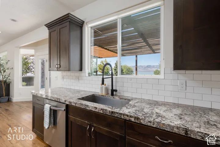 Dark wood-finish cabinetry, granite-style countertops, stainless steel dishwasher, white subway tile backsplash, and a black gooseneck faucet