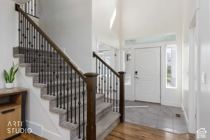 Two-story foyer featuring a white paneled entry door with sidelights, a transom window, and a carpeted staircase with dark wood-finish handrails and black iron balusters