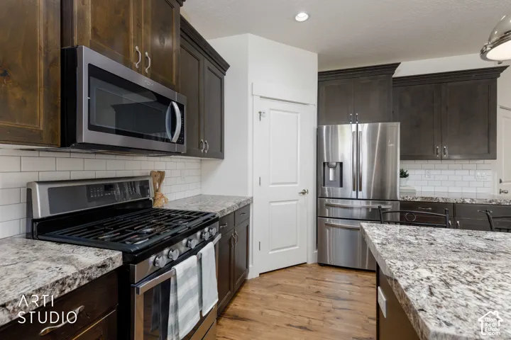 Gourmet kitchen featuring dark wood cabinetry, stainless steel appliances, a subway tile backsplash, and light-toned countertops