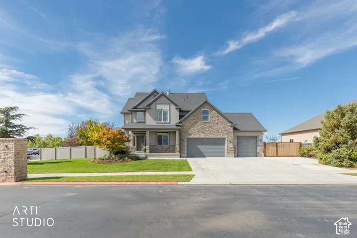 Exterior featuring stone and siding finishes, a two-car garage, a single-car garage, a manicured lawn, and a paved driveway
