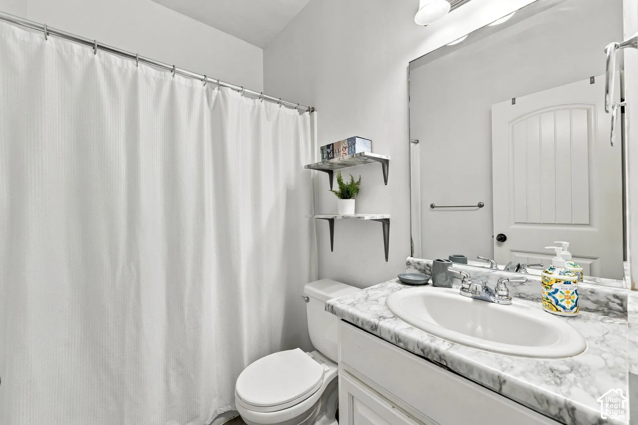 Vanity with an integrated sink and a marbled-finish countertop, large wall mirror, and a white toilet
