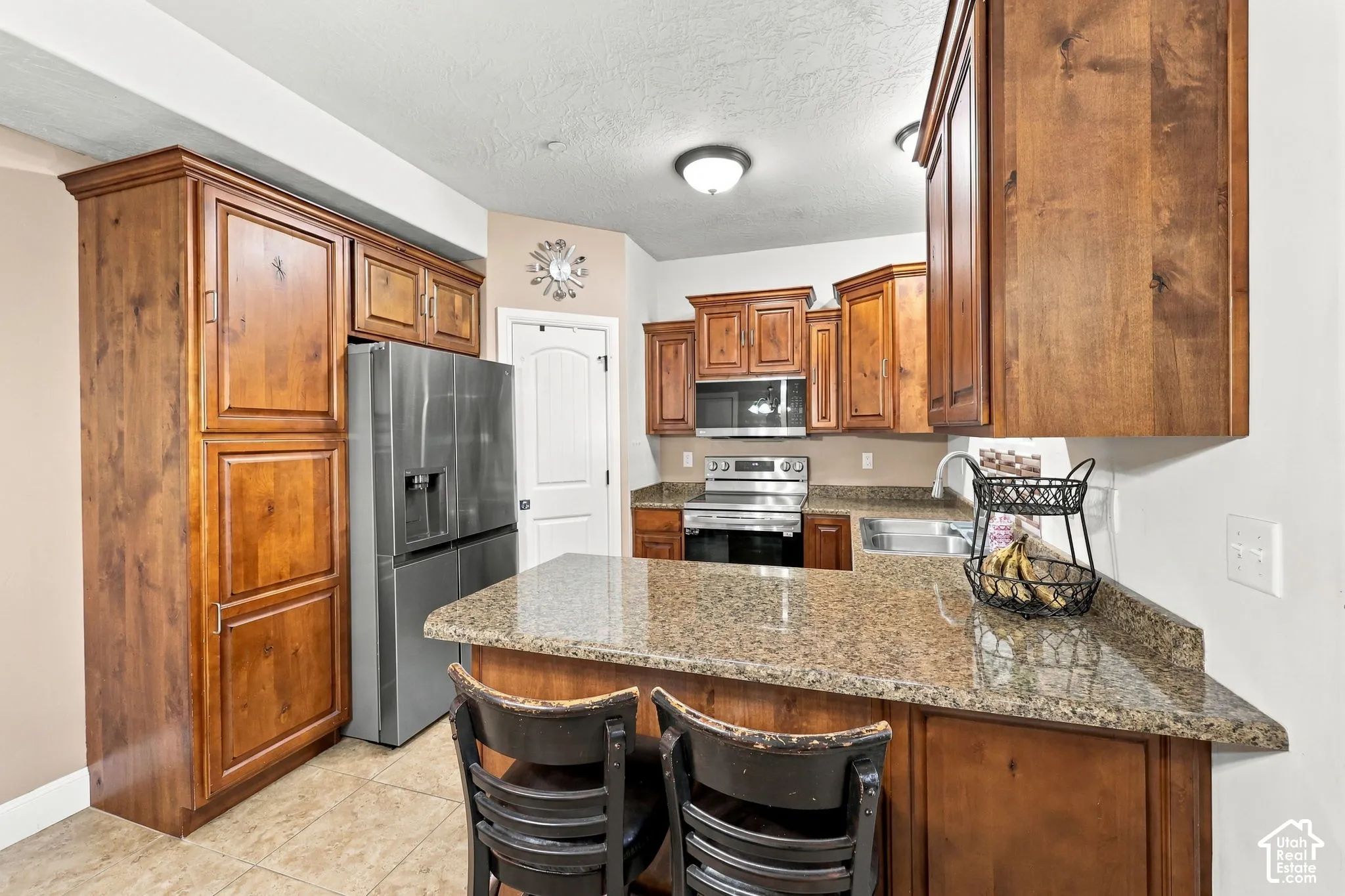 Kitchen featuring wood cabinetry, stainless steel appliances, a bar-height countertop, a stainless steel sink, and tiled flooring