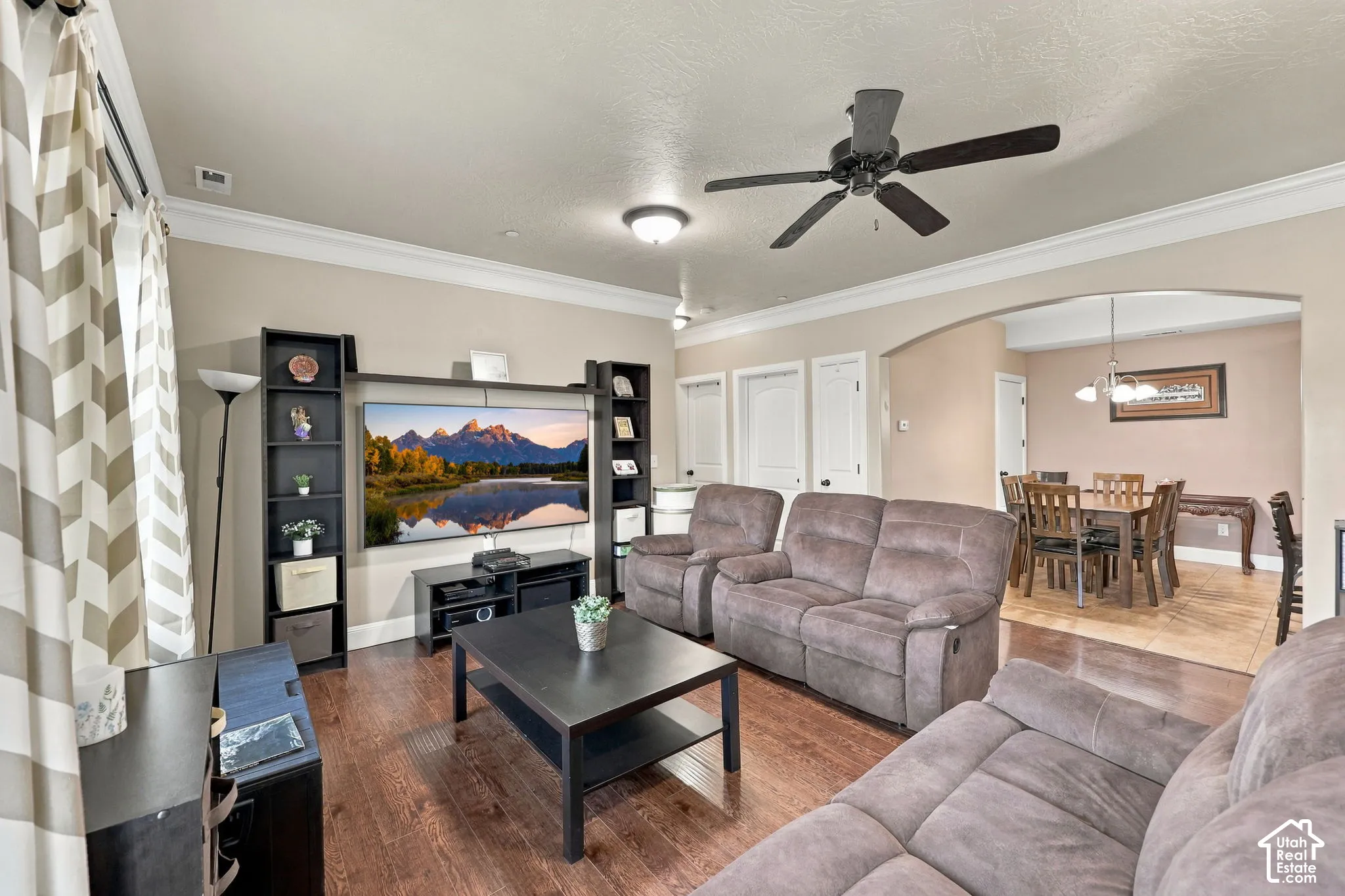 Spacious living area featuring wood-finish flooring, a ceiling fan, and crown molding