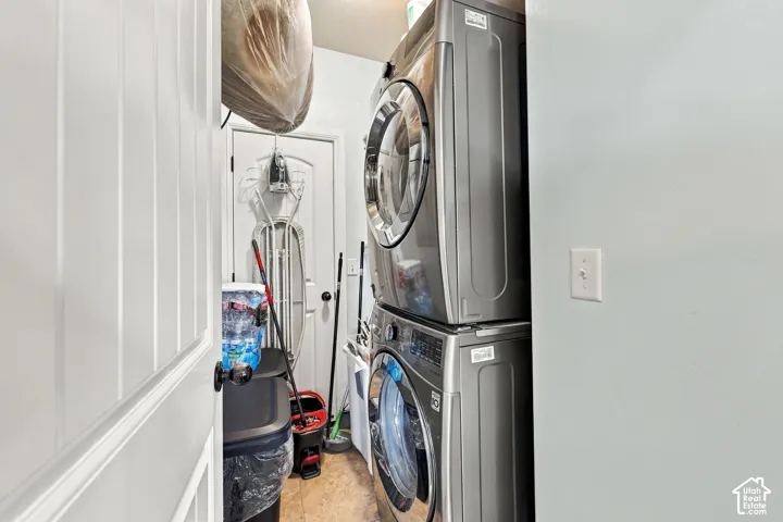 Laundry area with stacked washing machine and dryer, paneled door, and durable flooring