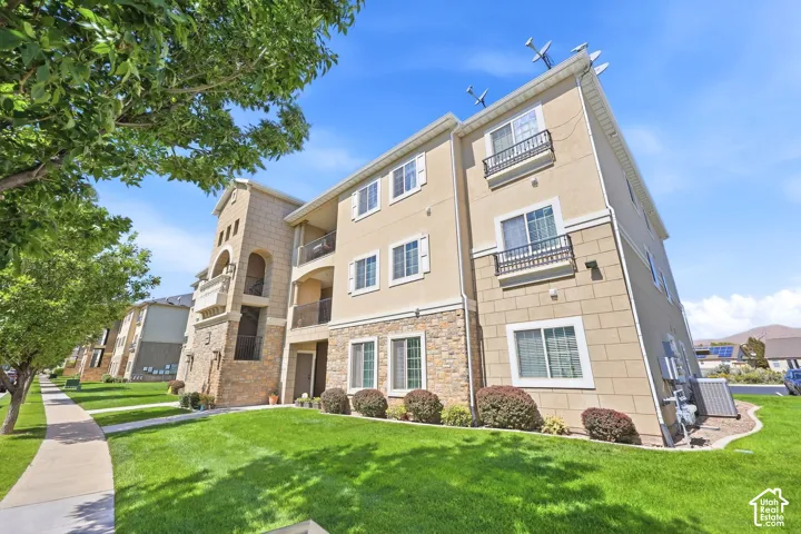 Multi-story building featuring a stucco and stone exterior with decorative balconies, manicured lawn, and mature trees