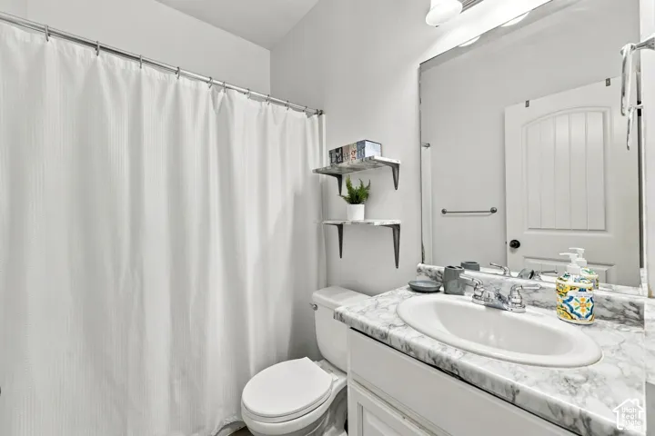 Vanity with an integrated sink and a marbled-finish countertop, large wall mirror, and a white toilet