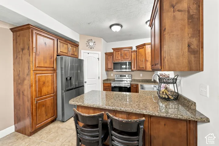 Kitchen featuring wood cabinetry, stainless steel appliances, a bar-height countertop, a stainless steel sink, and tiled flooring