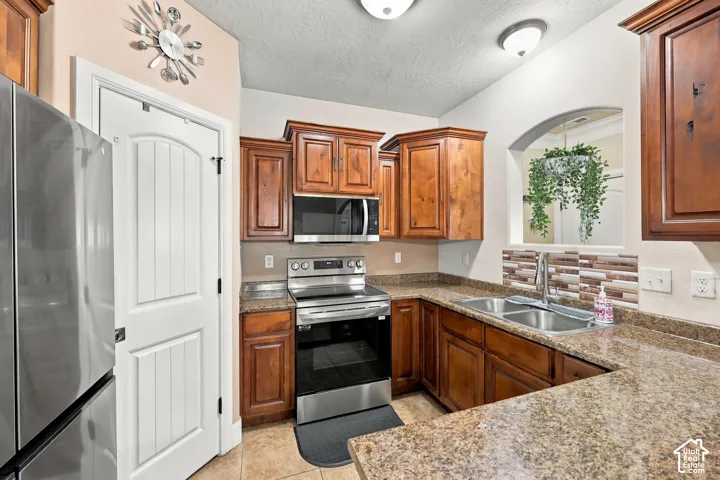 Kitchen featuring wood cabinetry, stainless steel appliances, a multi-tone tile backsplash, a double basin sink, and ample counter space