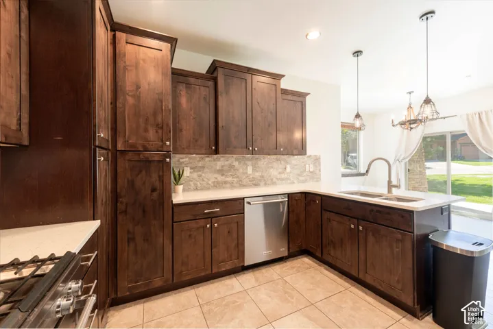 Kitchen featuring dark wood cabinetry, light-toned countertops, tile flooring, stainless steel appliances, and a double basin sink with a gooseneck faucet