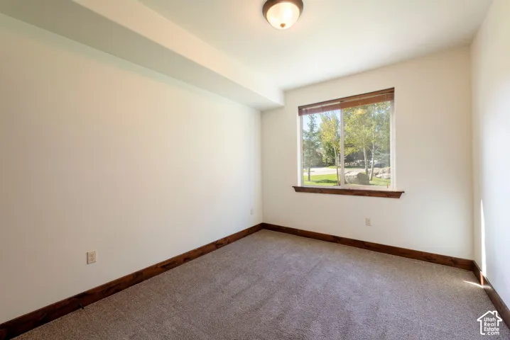 Neutral wall finishes, recessed ceiling beam, large window with wood trim, carpeted flooring, and a flush mount ceiling light fixture