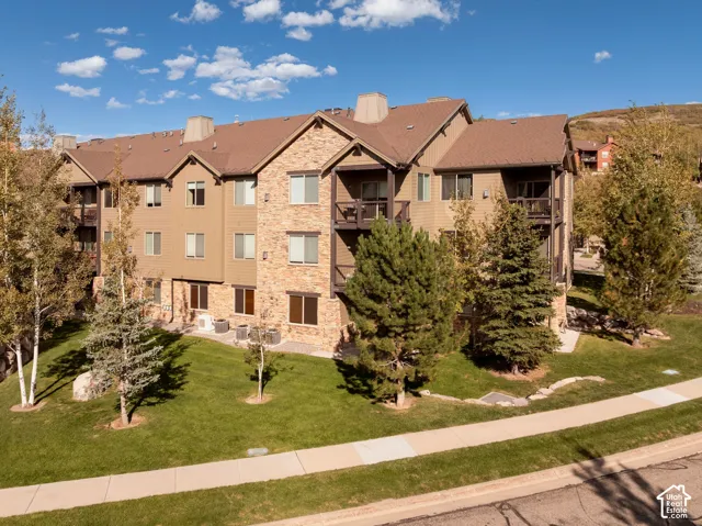 Multi-level exterior with stone and siding facade, private balconies, and surrounding mature trees and manicured lawn