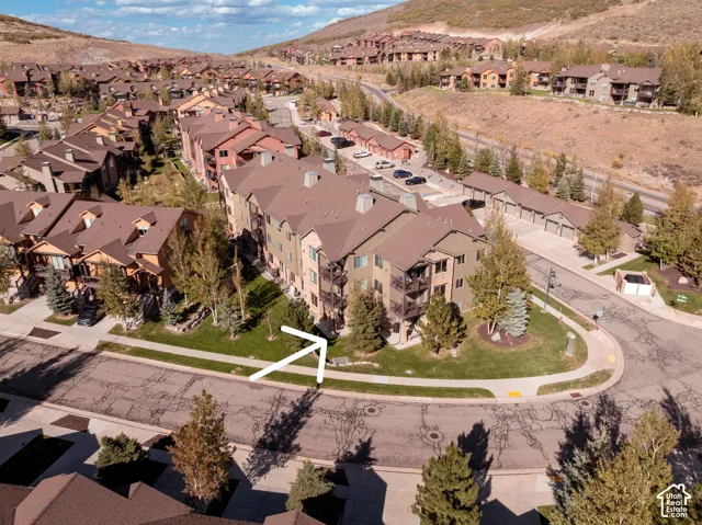 Multi-story building with multiple balconies and a pitched roof, surrounded by paved roads and mature landscaping