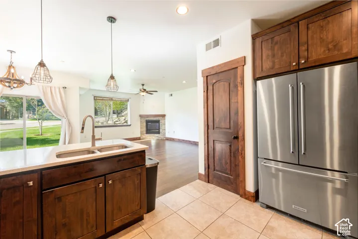 Kitchen island with an undermount dual-basin sink and a gooseneck faucet, stainless steel French door refrigerator, wood-finish cabinetry, and tiled flooring