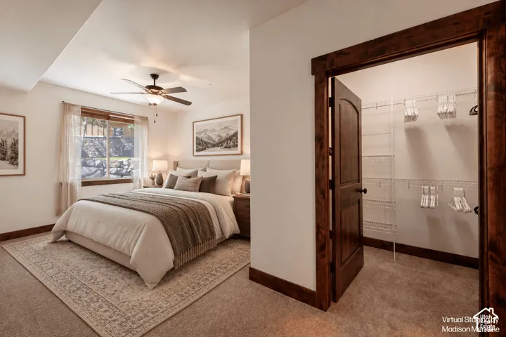 Carpeted bedroom with a ceiling fan, a window featuring wood trim, and a closet with wire shelving