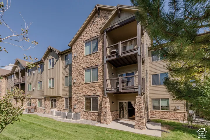 Multi-story building exterior featuring stone and siding finishes, multiple balconies with dark wood railings, and a ground-level patio