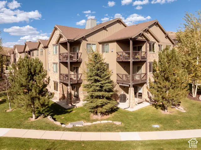 Multi-story building featuring stone veneer accents, multiple private balconies with wood railings, and a lower-level patio