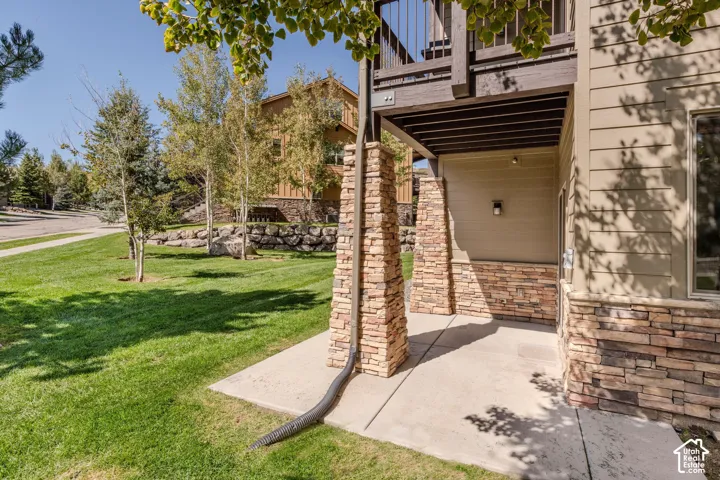Covered patio with stone veneer columns and siding, concrete flooring, and an expansive lawn