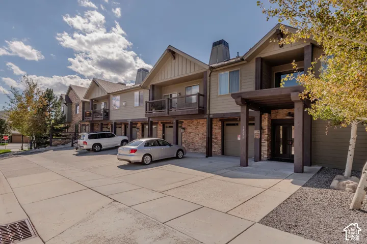 Townhome exterior featuring gabled roofs, stone accents, private balconies, an attached garage, and a covered entry