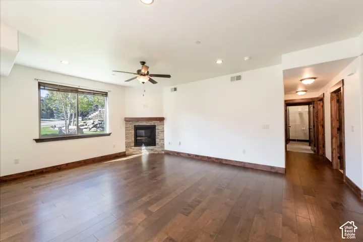Hardwood flooring, corner fireplace with stone surround, wood mantel, ceiling fan, and recessed lighting