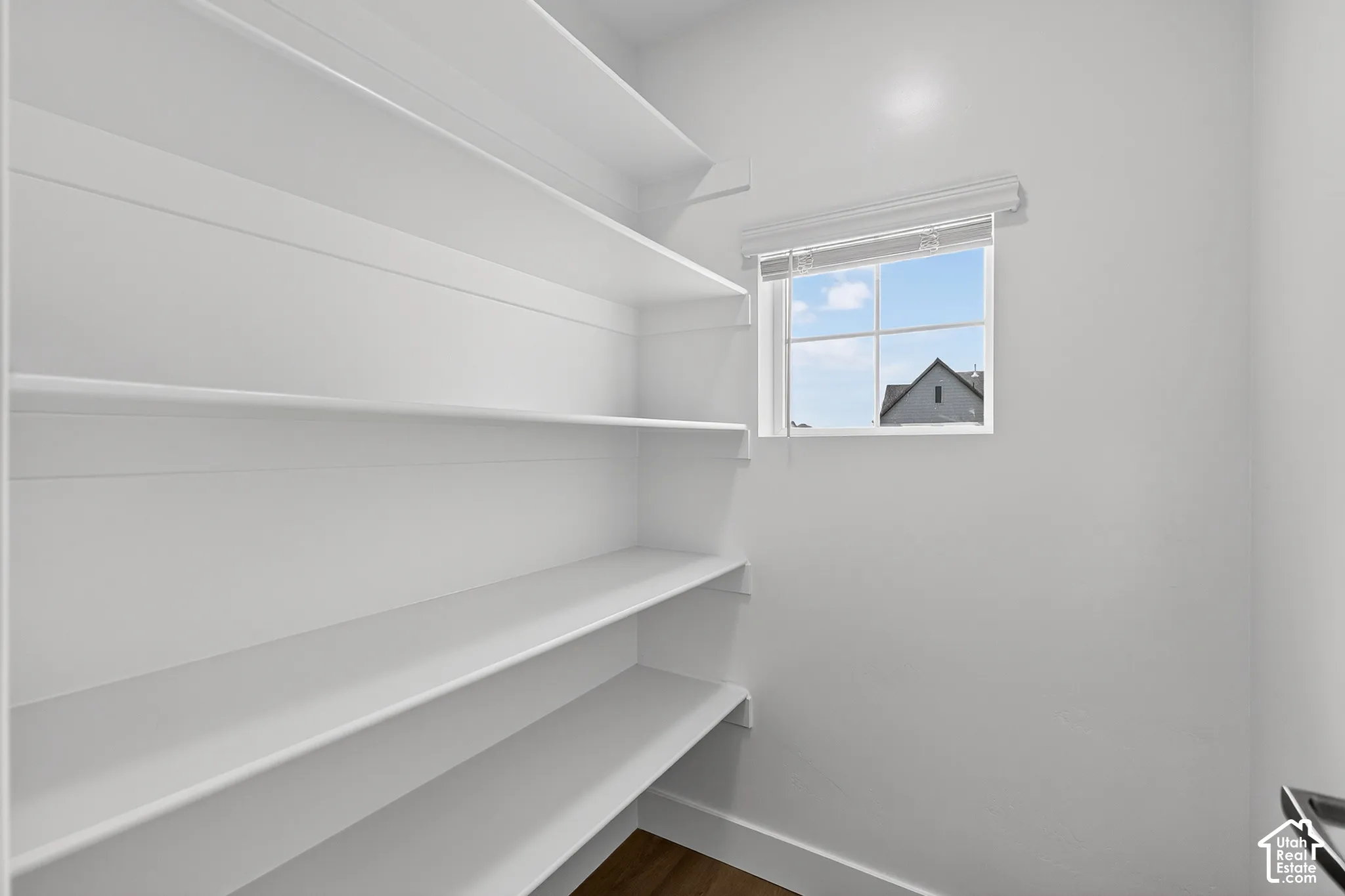 Bright, organized pantry featuring multiple built-in shelves with clean white finishes, ample storage capacity, and a window with natural light and exterior sightlines