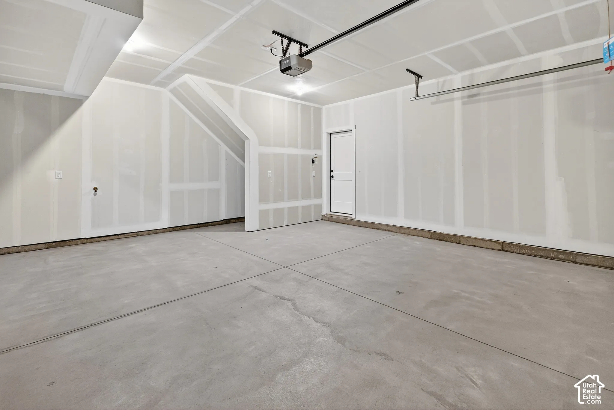 Unfinished interior garage with concrete flooring, exposed drywall, overhead garage door track system, and an interior access door