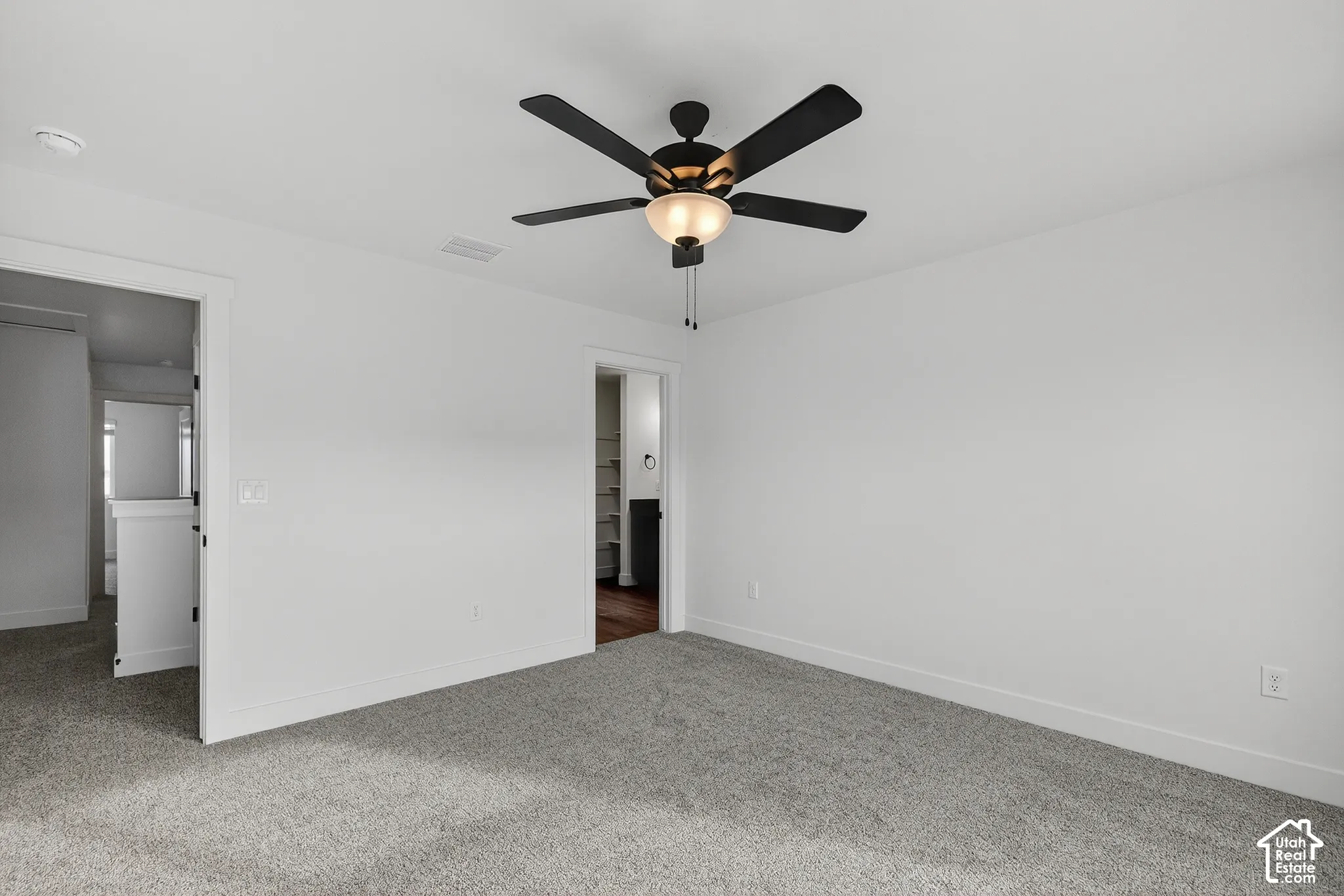 Neutral-toned wall paint and trim, textured gray carpeting, and a ceiling fan with light fixture