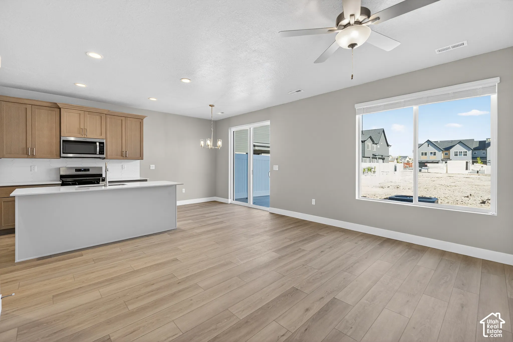 Wood-finish flooring throughout, kitchen island with sink, stainless steel appliances, recessed lighting, and a ceiling fan