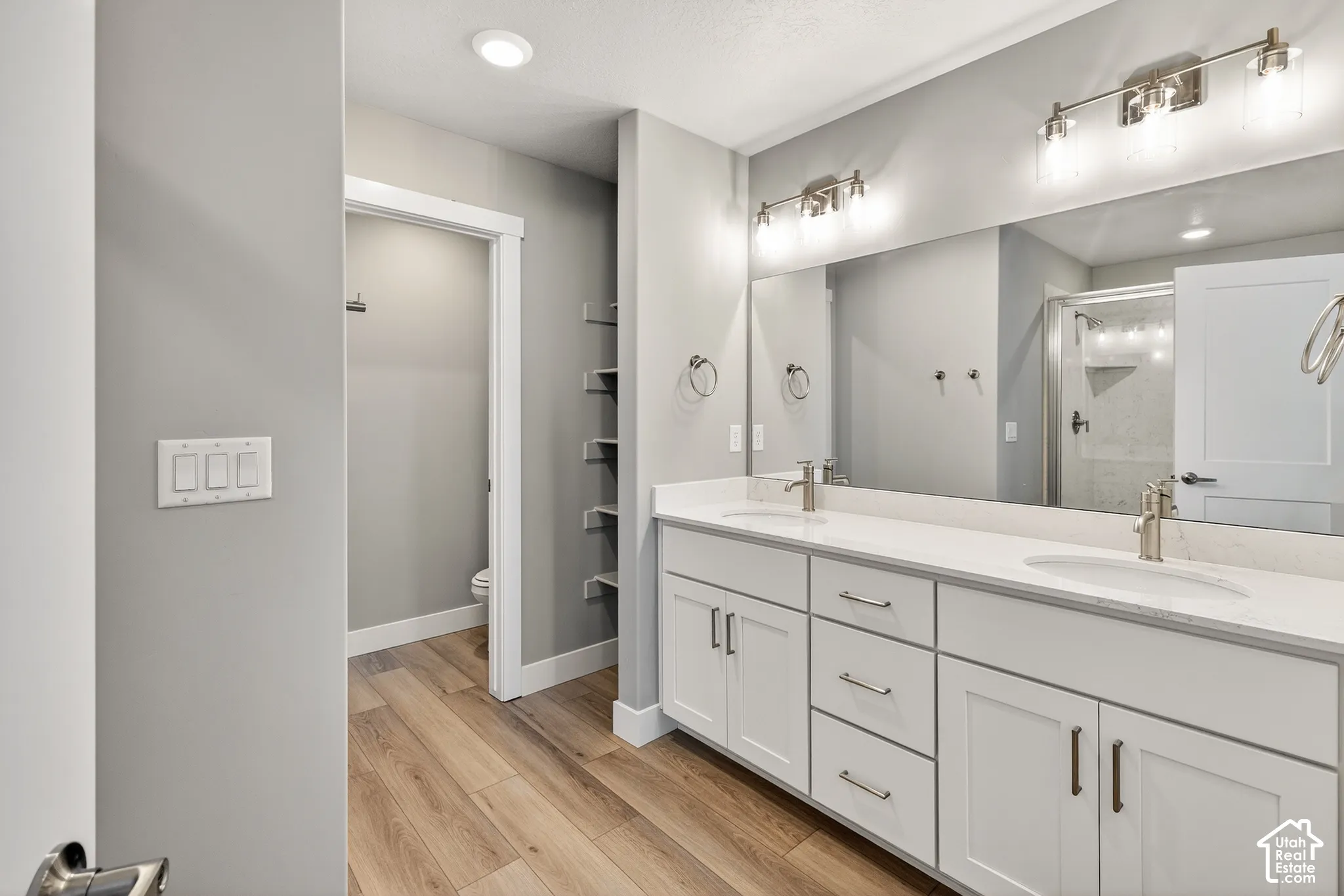 Double vanity with undermount sinks, wood-finish flooring, white cabinetry with brushed nickel hardware, and a large wall-mounted mirror