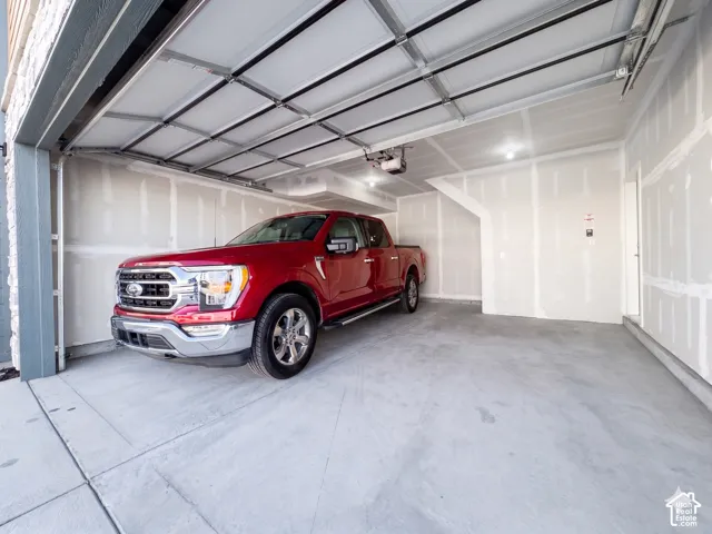 Spacious garage with an automatic overhead door, concrete flooring, and ceiling-mounted lighting