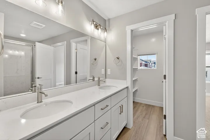 Dual vanity with integrated sinks and brushed nickel faucets, a full-width mirror, and a walk-in shower with a glass enclosure