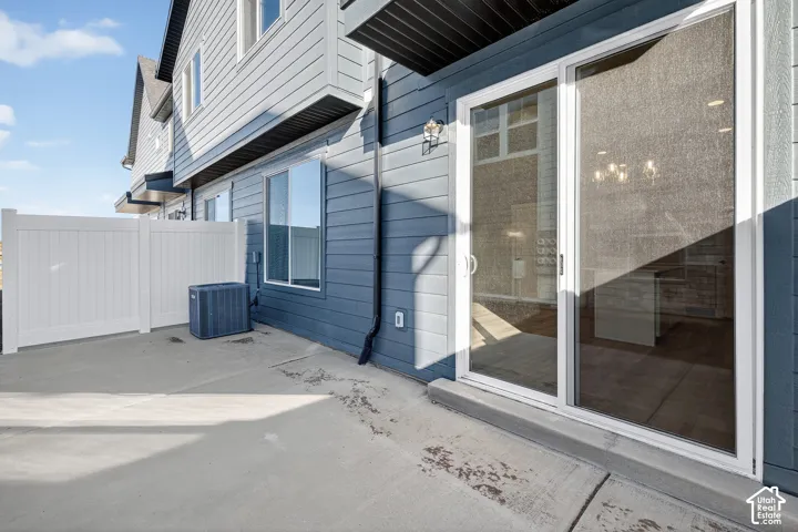 Concrete patio with a white privacy fence, sliding glass doors, and exterior wall lighting