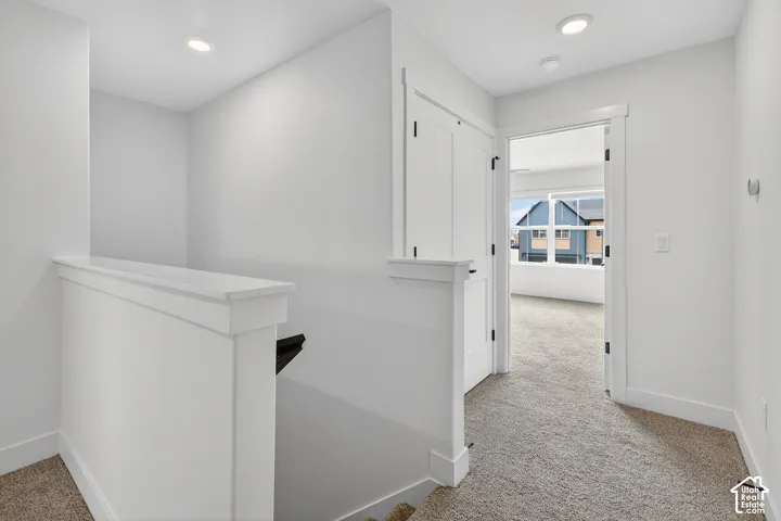 Carpeted hallway with recessed lighting, white trim, and a contemporary door frame opening to a room with large windows