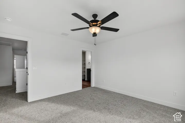Neutral-toned wall paint and trim, textured gray carpeting, and a ceiling fan with light fixture