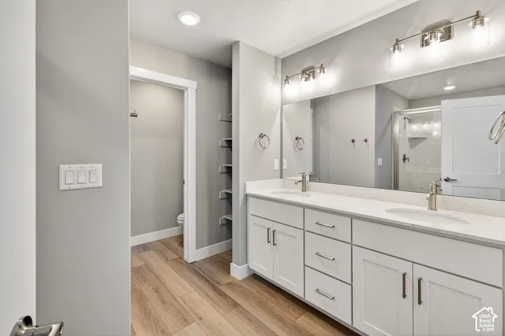 Double vanity with undermount sinks, wood-finish flooring, white cabinetry with brushed nickel hardware, and a large wall-mounted mirror