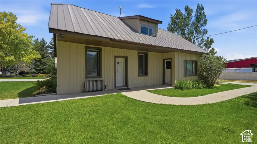 Light-colored exterior siding with dark trim, featuring a metal roof and an upper dormer window