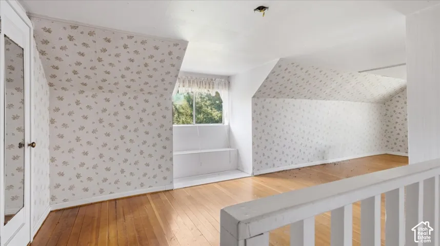 Hardwood flooring, painted railing, built-in shelving, window with natural light, and a closet with a mirrored door