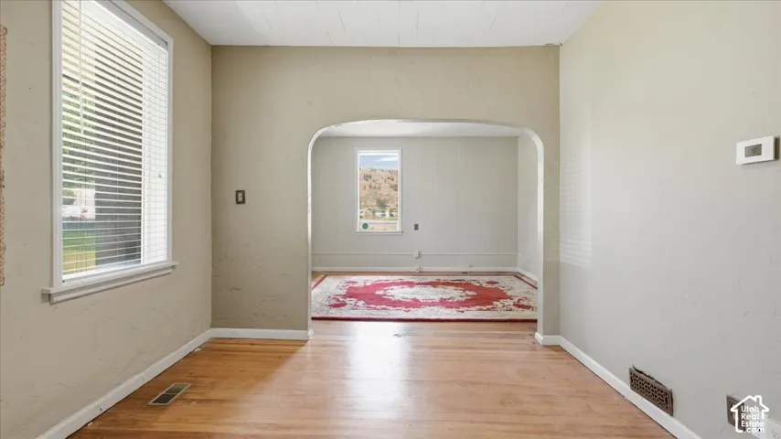 Hardwood flooring, arched doorway, window with blinds, textured wall finish, and a thermostat