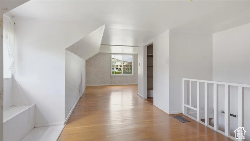 Wood-finish flooring throughout, white painted walls, window with a built-in window seat, and an open doorway leading to an additional space