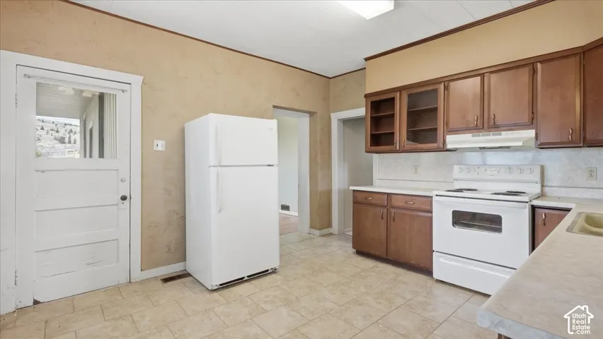 Kitchen featuring wood cabinetry, white appliances, and a tile floor