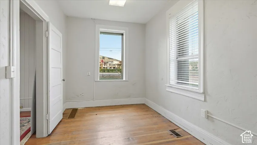 Wood-finish flooring with white baseboards, white paneled door, and white window trim