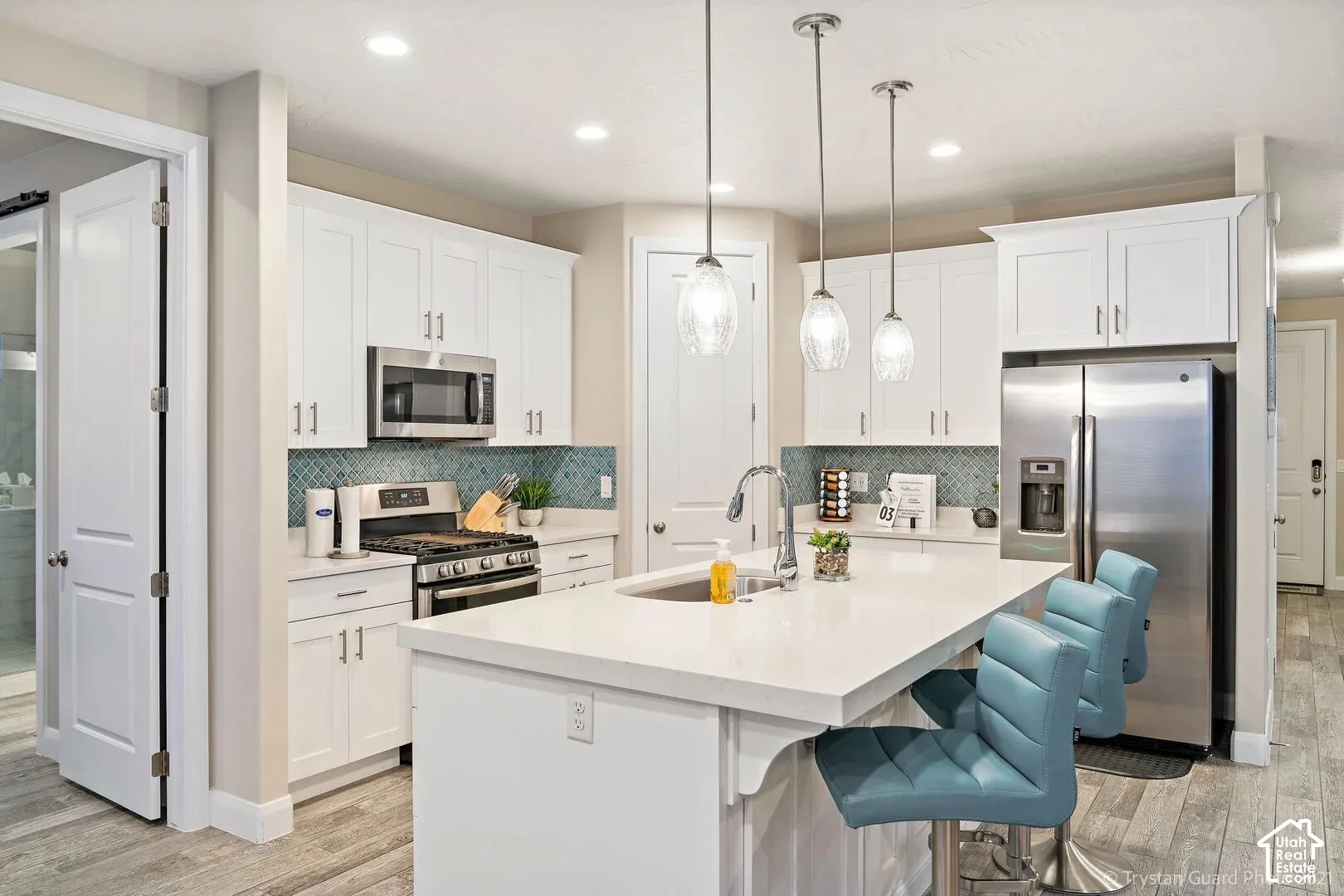 White cabinetry, stainless steel appliances, patterned tile backsplash, recessed lighting, and tile flooring