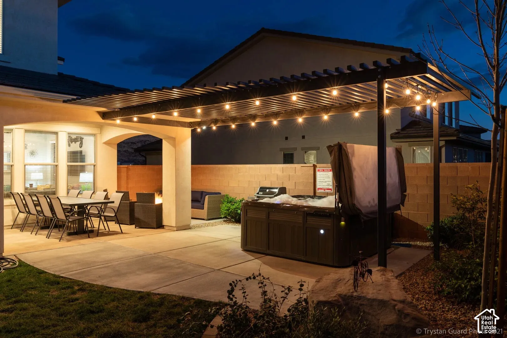 Expansive concrete patio with a covered outdoor dining area, a built-in spa, a fire pit, and string lighting