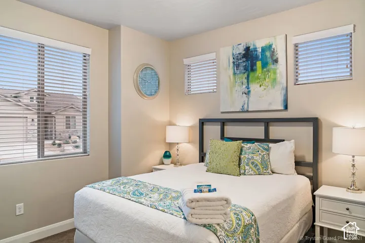 Light-toned walls, multiple windows with blinds, a metal bed frame, and carpet flooring